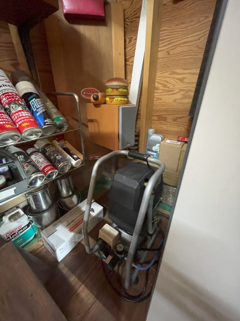 ガレージ内の奥側に設置されたエアコンプレッサー本体の様子。ケミカル品置台と一緒の風景