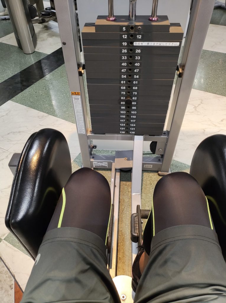 トレーニングマシンで脚を開く動作前の様子。太もも外側を鍛える運動シーン