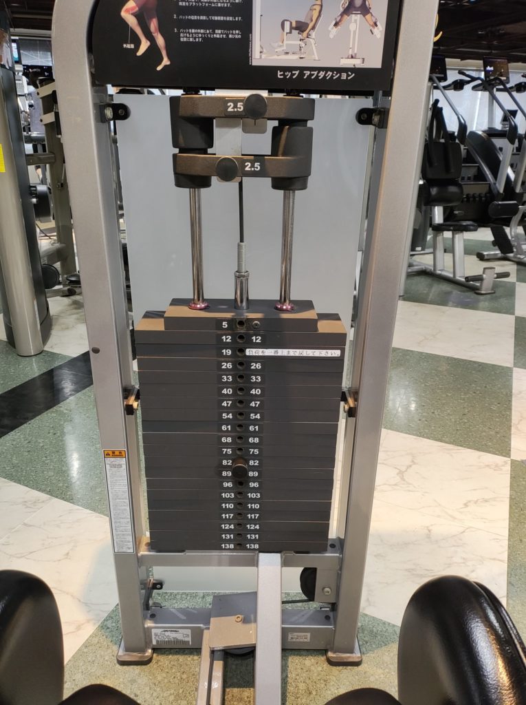 ジムのヒップアブダクションマシン。お尻の横の筋肉（中殿筋・小殿筋）を鍛えるトレーニングに使用されるマシンの全体写真。