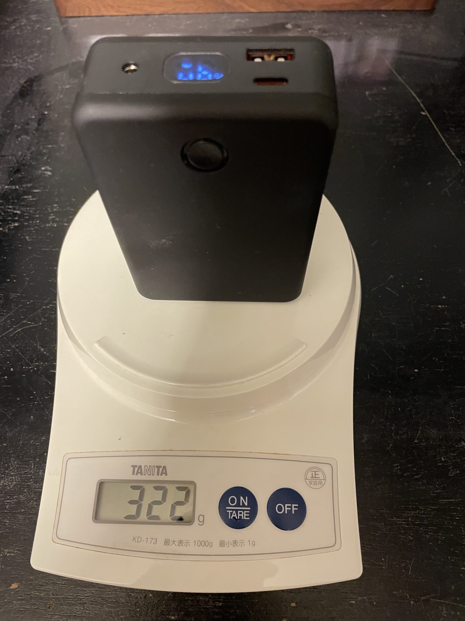 付属のバッテリー画像と重量を計測している画像。指示値は322ｇを指している