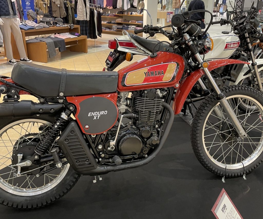 1976年式 YAMAHA XT500 がショッピングモールの展示スペースに並んでいる様子。空冷シングルエンジンとドライサンプ構造が特徴のクラシックオフロードバイク。